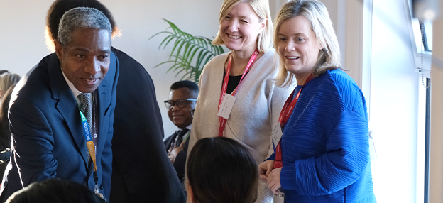 Staff member of the College greeting with handshake while two other people look on smiling
