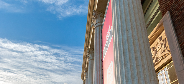 College pillars against a blue, cloudy sky with orange from sunset spilling across